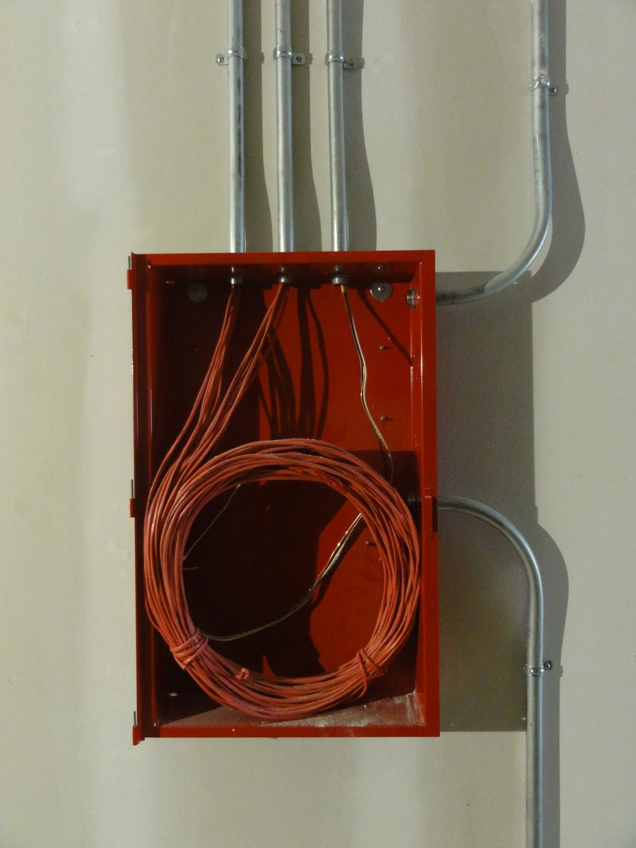 Open junction box mounted on a wall with a coiled bundle of cable and conduit runs