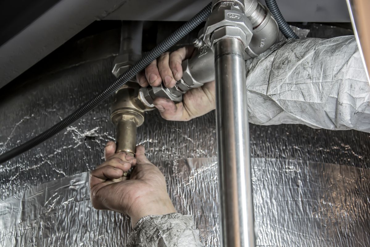 Hands connecting a braided supply hose fitting to insulated pipework