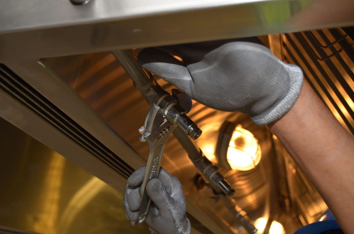 Gloved hand using an adjustable wrench on a brass pipe fitting
