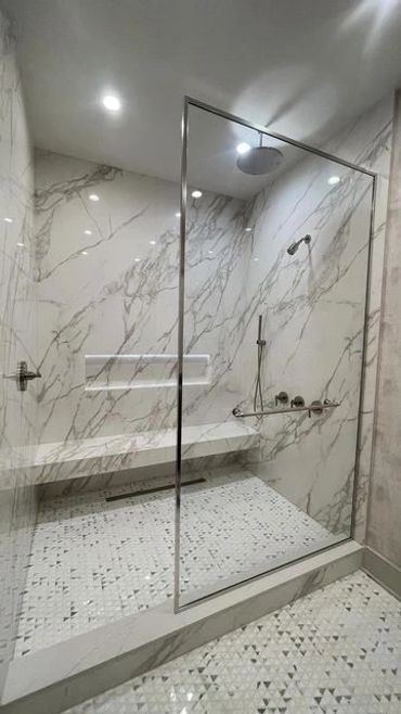 Fully retiled marble shower with a glass enclosure and built-in bench